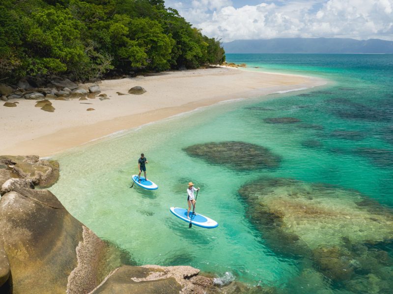 an aerial shot of two people stand-up paddling on the clear turquoise waters of Nudey Beach, Fitzroy Island